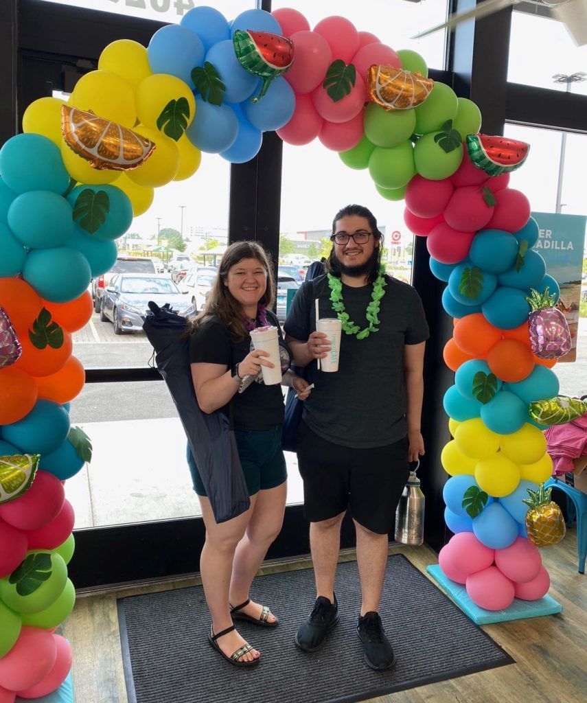 Guest at Grand Opening with smoothies under a balloon arch