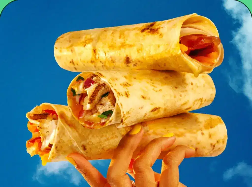 A hand holding three toasted wraps against a blue sky