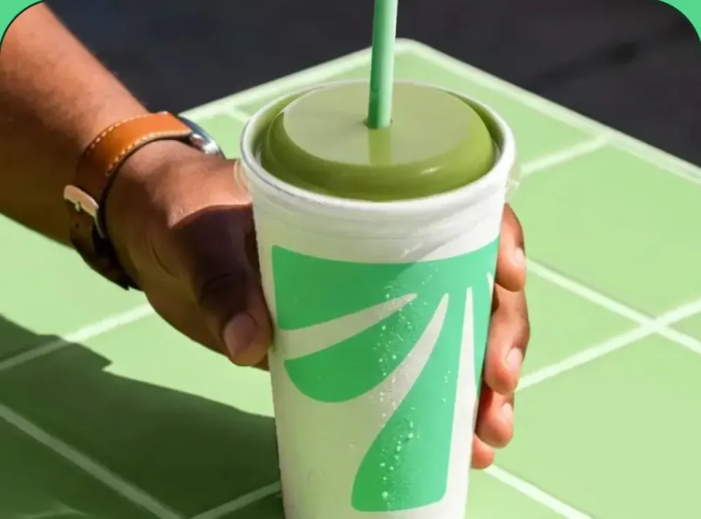 A hand setting a Tropical Smoothie Cafe cup on a green tiled table